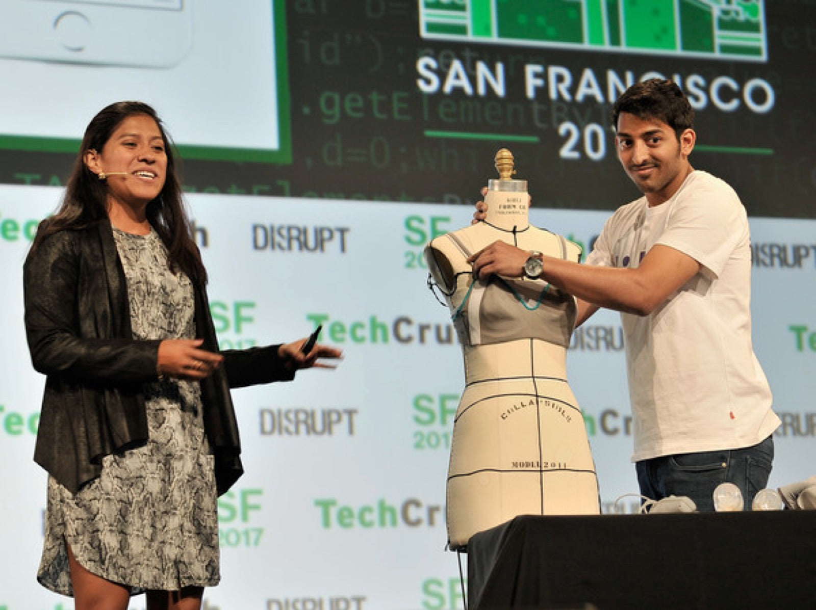 Adriana presenting on stage at TechCrunch Disrupt while Sujay demonstrates the Lilu Massage Bra on a dress form.