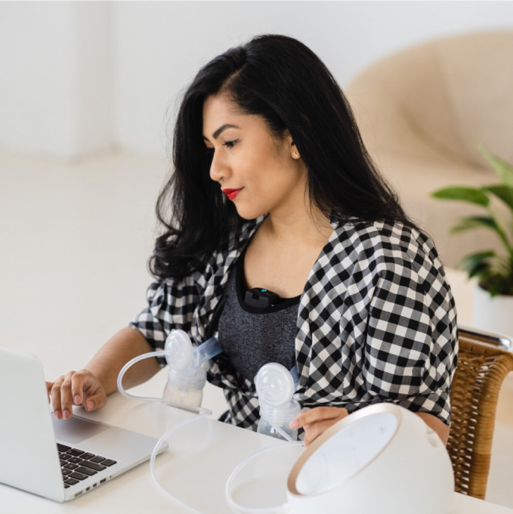A pumping parent using the Lilu Massage Bra while working at a laptop.